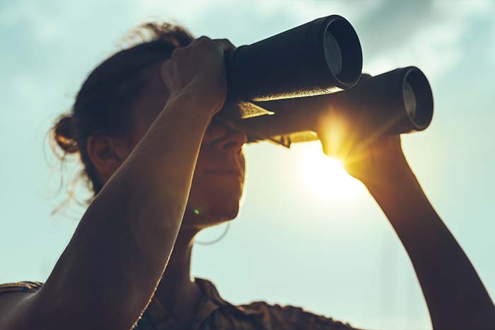 a man looking through binoculars at sunset
